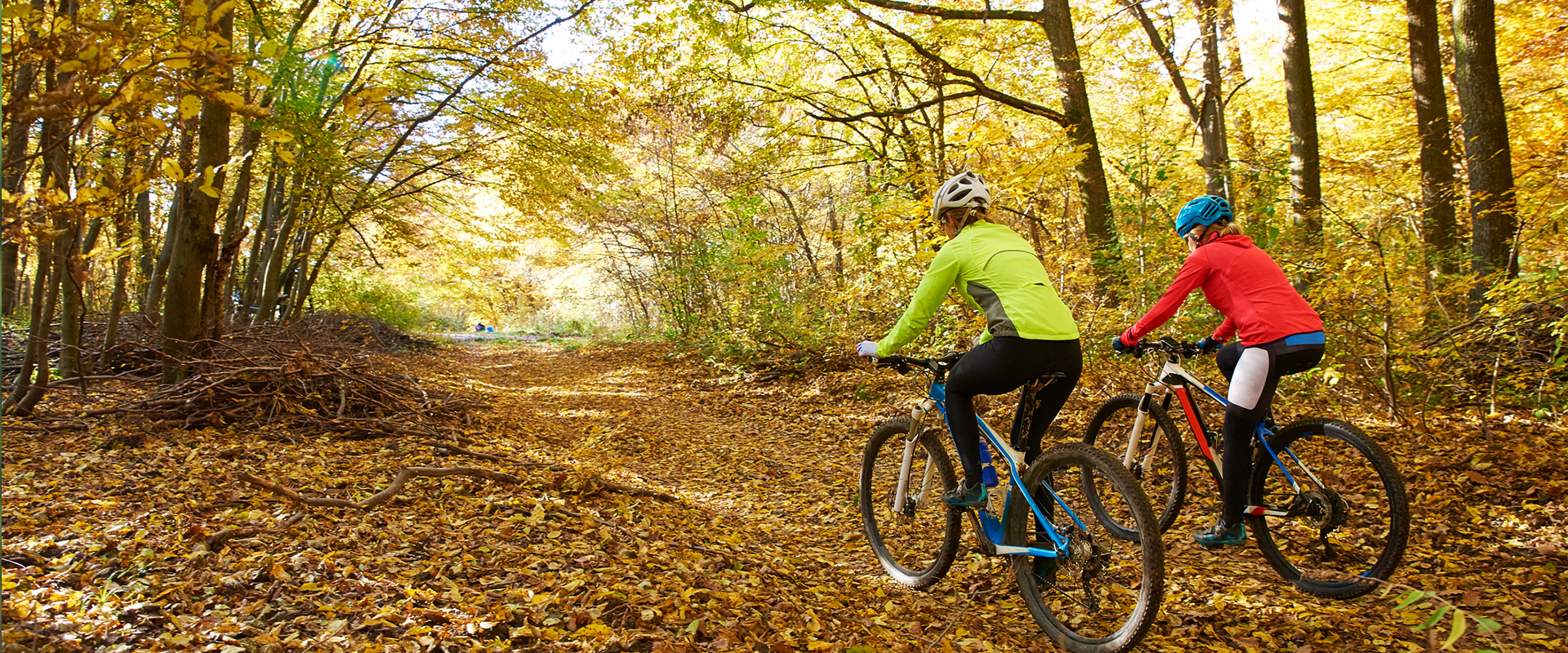 Two female cyclists cycling through trail with fallen leaves