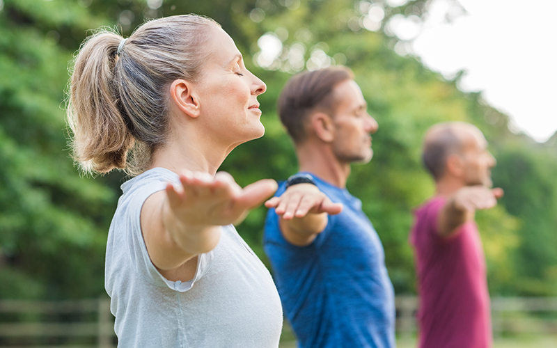 Group of three people practicing yoga outdoors - mobile