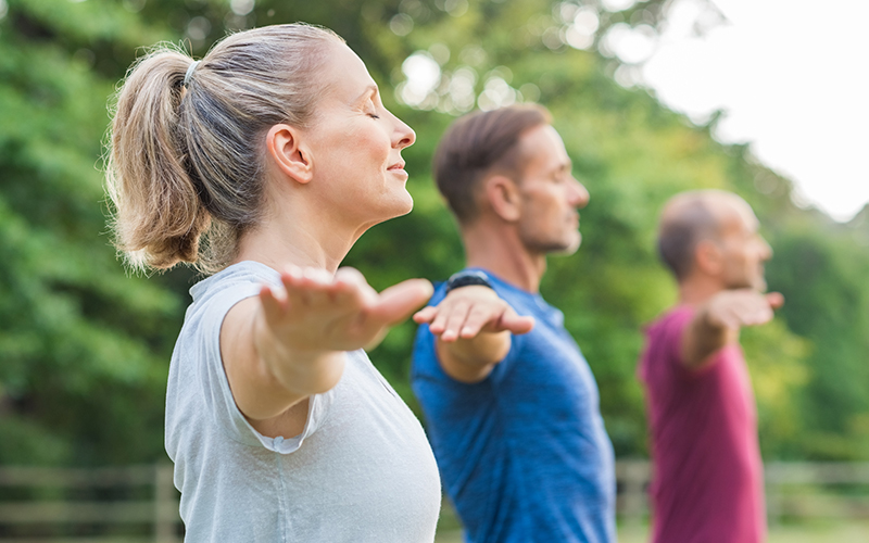 Group of three people practicing yoga outdoors - mobile version